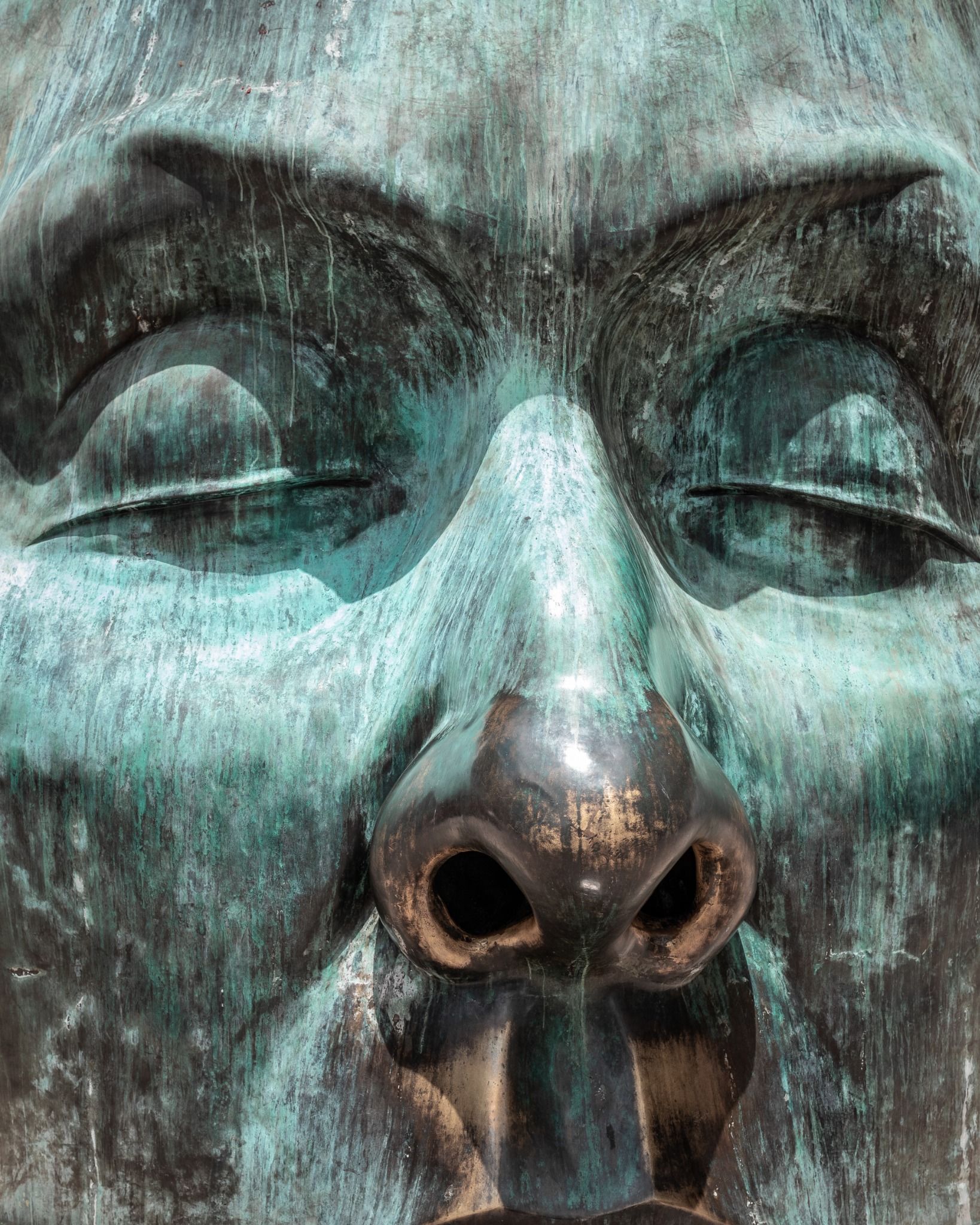 Close-up of a bronze sculpture face with green patina